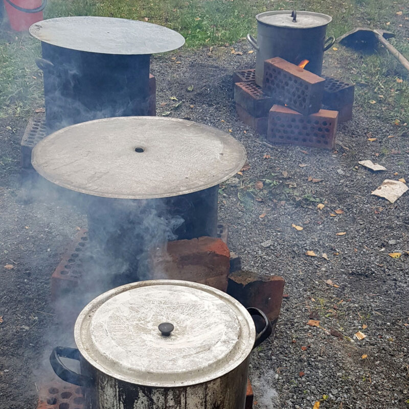 Höyryävät kattilat tiilistä tehtyjen nuotioiden päällä.